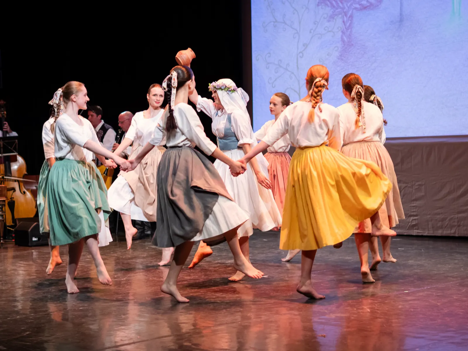 Girls in folk costumes dancing in a circle with flower wreaths